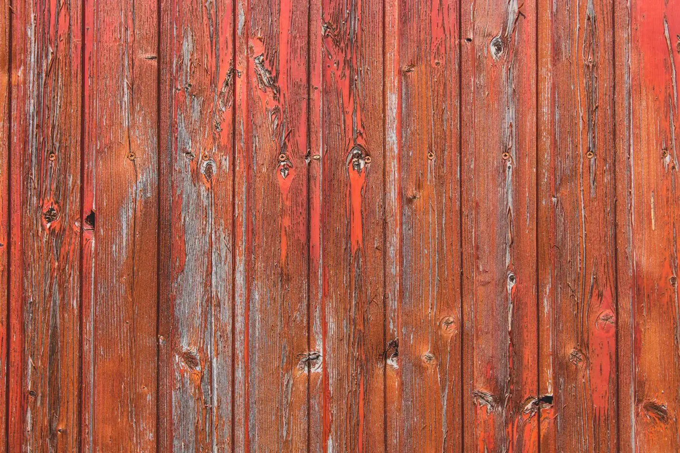Weathered vertical timber boards with peeling red paint